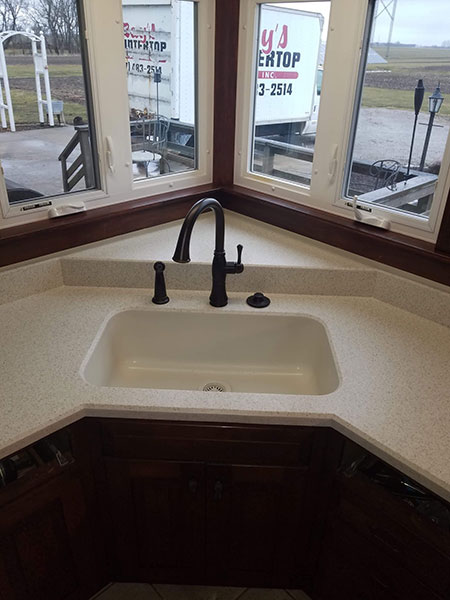 A single basin corner sink with a modern black faucet in a residential home in Glenarm, IL installed with a new white countertop.