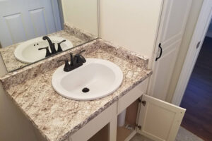 A white and brown bathroom laminate countertop with a new sink and black faucet installed by countertop professionals at Ray’s in Glenarm, IL.