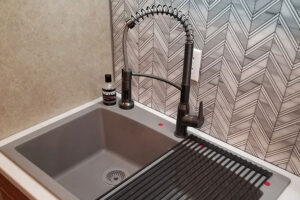 A dual basin sink with a roll-up rack next to the sink and countertop in Glenarm, IL. A small kitchen sink and countertop with a black faucet and white and grey backsplash.