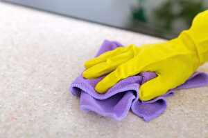 A person wearing a yellow rubber glove and holding a purple cloth rag cleaning their granite countertop with professional cleaning accessories in Glenarm, IL.