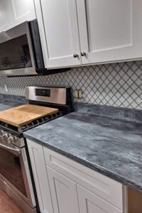 A grey and white solid surface countertop installed in a Rochester, IL kitchen with white cabinets and a tile backsplash.
