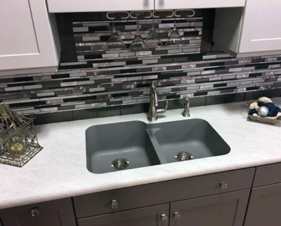 A grey quartz sink installed on a beautiful white countertop and grey tile backsplash from Ray’s Countertop Shop in Glenarm, IL.