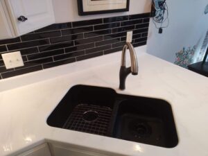 A modern black quartz countertop installed in Glenarm, IL with a stainless-steel faucet and black tile kitchen backsplash.