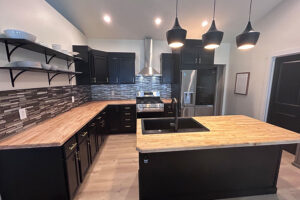 A butcher block countertop installed in a kitchen in Glenarm, IL with black cabinets and exposed shelving by Ray's Countertop Shop.