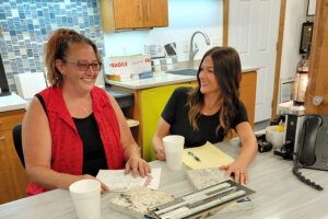 Two women sitting and laughing at a table while discussing stainless steel sink options for a kitchen in Springfield, IL.